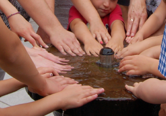 Kinder halten Hände in Taufbrunnen