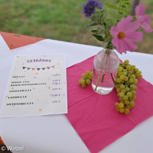 Blumenvase steht auf einm Biertisch und danaben liegt die Speisekarte für das Gemeindefest
